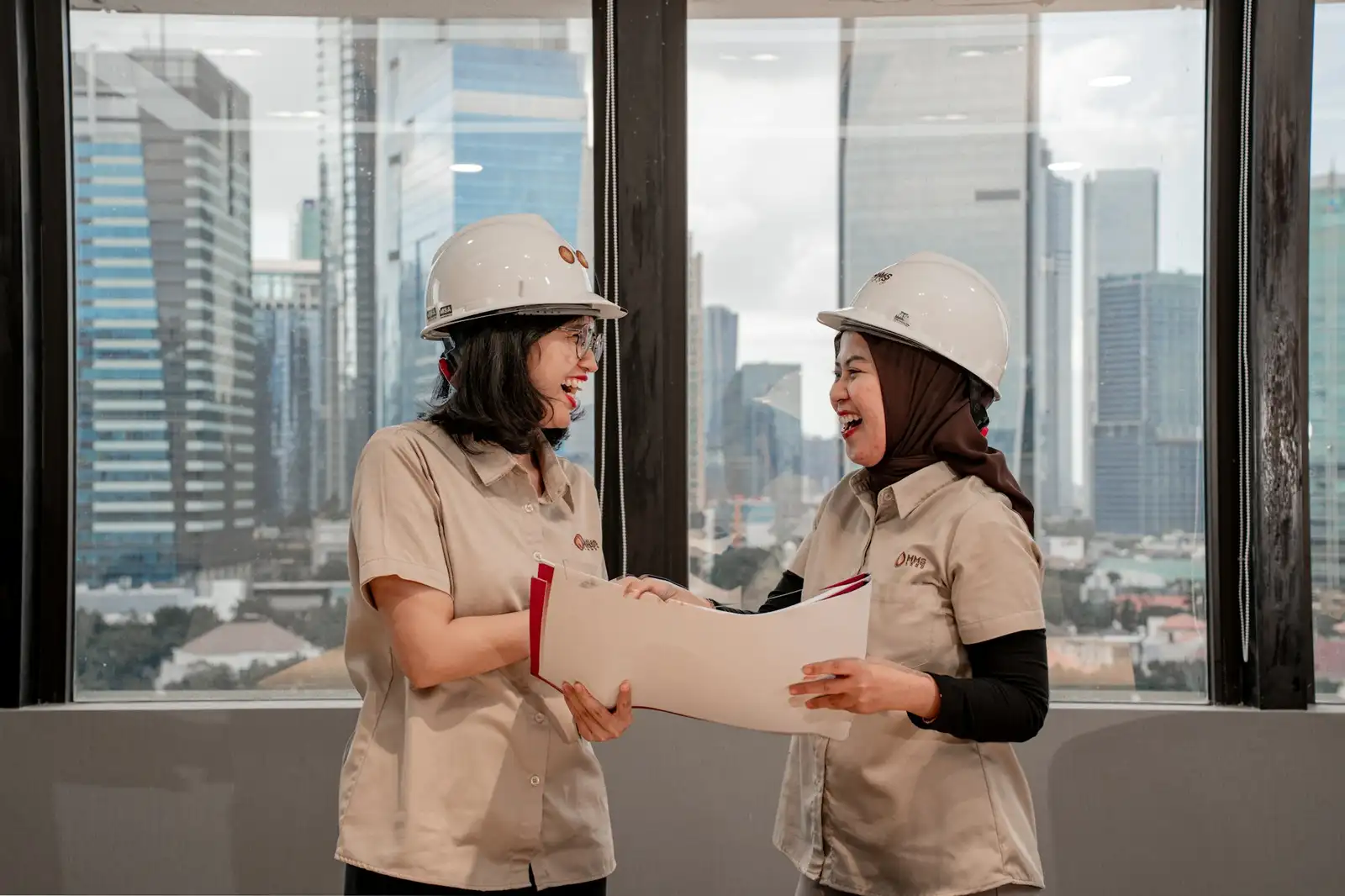 Two people in hard hats reviewing plans by a window