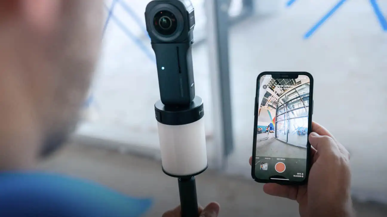 A 360° camera on a selfie stick, with a phone showing the live view