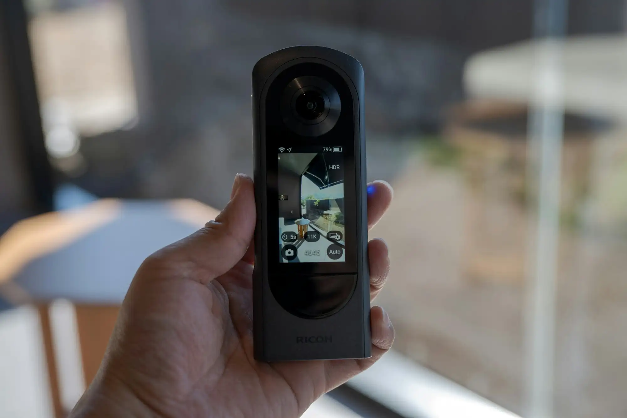 A hand holding a 360 camera in front of a window