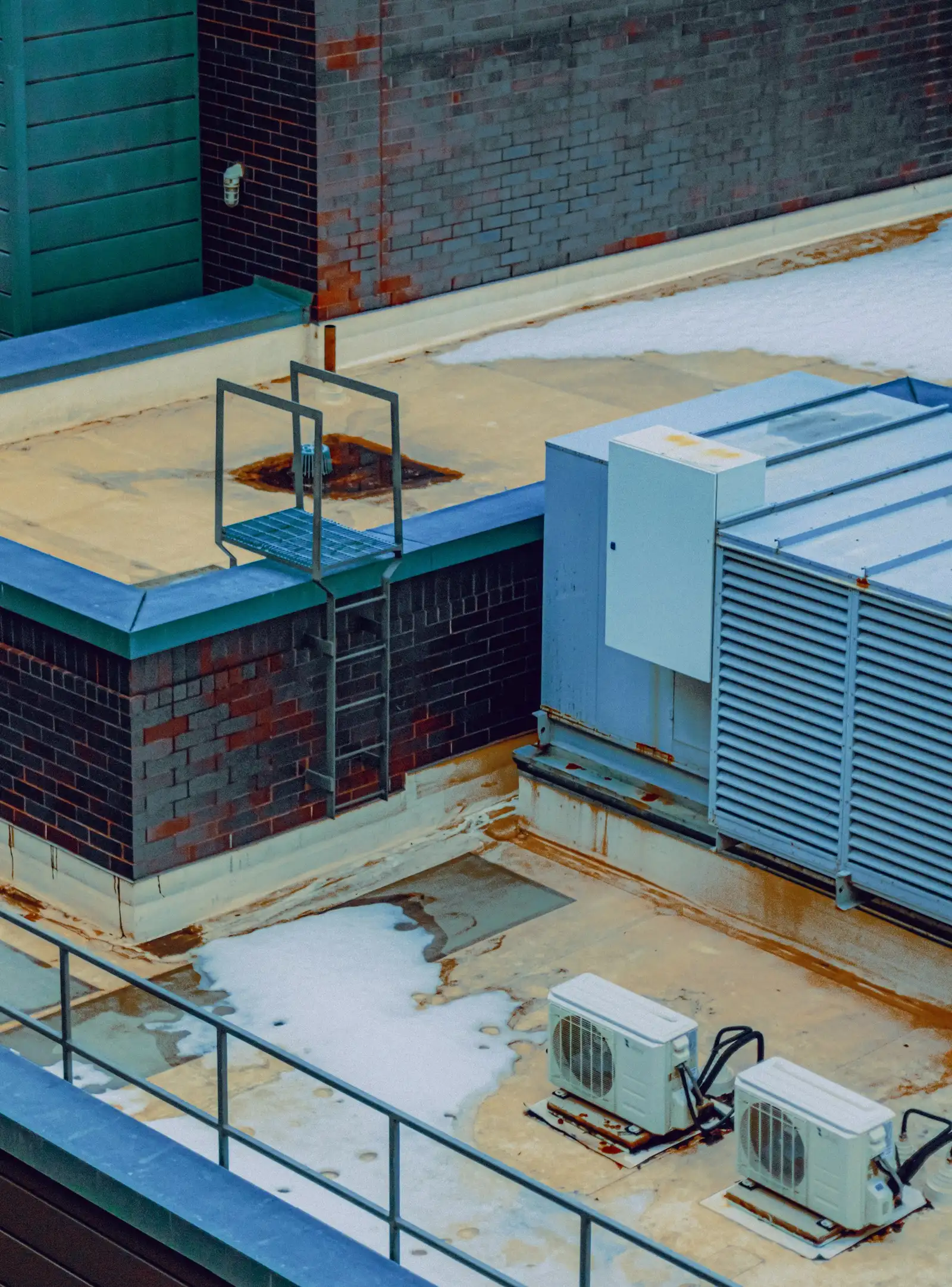 A commercial rooftop with a rooftop unit, a drain, a ladder and condensing units